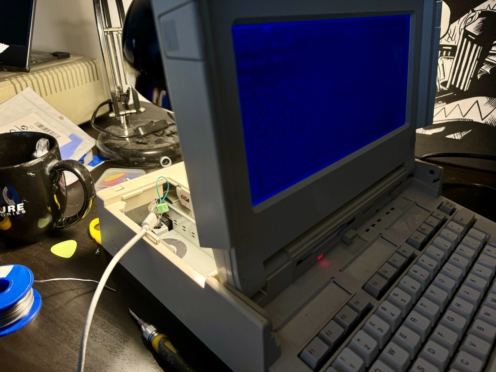 A USB-C cable hooked up to a small circuit board hooked
up to the battery terminals of the open battery bay of a Tandy 1400 LT
luggable. The Tandy is switched on